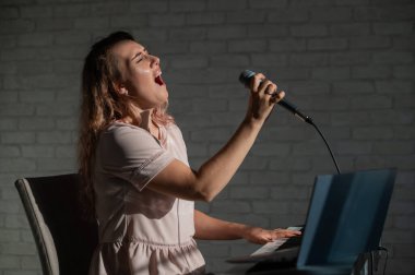 Etkileyici bayan şarkıcının dizüstü bilgisayarında bir video blogu var. Web kamerasıyla şarkı kaydeden ve bir sentezleyiciyle beste yapan bir kızın portresi. Online müzik dersleri. Karantinada mesafe öğrenimi.