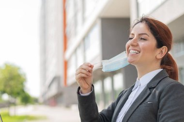 Sosyal mesafeyi korurken dışarıda dizüstü bilgisayarda çalışan tatmin olmuş bir kadın. Gülümseyen kadın ofis çalışanı kafede otururken özgürlüğün tadını çıkarıyor. Coronavirus yenildi. Maskeni çıkar..