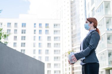 Mutsuz kovulmuş maskeli kadın elinde kişisel eşyalarla caddede duruyor. Dışarıdaki işsiz ve çaresiz bir kadının portresi. Küresel ekonomik kriz.