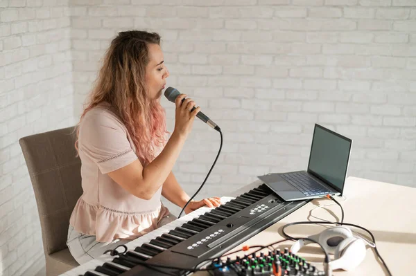 Een vrouw neemt een zangles op met een laptop en begeleidt thuis op een toetsenbord. De leraar zingt een liedje in de microfoon en speelt elektronische piano. Een blogger neemt een video op. — Stockfoto