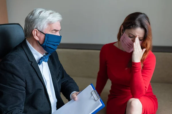 Male psychotherapist advises a female client in a medical mask. Moral support during the epidemic. Depressed woman on a visit to a psychologist. Treatment of panic attacks in the coronavirus.