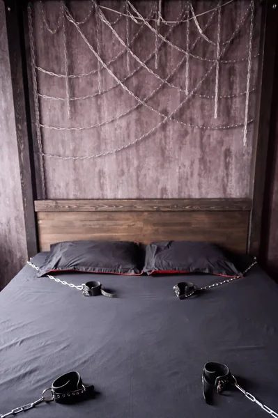 Schlafzimmer für intime Treffen. VDSM-Ausrüstung und Sexspielzeug. Lederhandschellen mit Kette auf einem grauen Laken. Fünfzig Grautöne. Fetisch-Dominanz. — Stockfoto