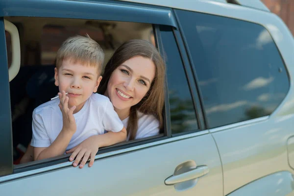 Bütün aileyle arabayla seyahat etmek. Oğlu gülümseyen mutlu beyaz kadın bir cipin arka koltuğunda oturmuş pencereden dışarı bakıyor. Yaz tatilinde araba gezisi. — Stok fotoğraf