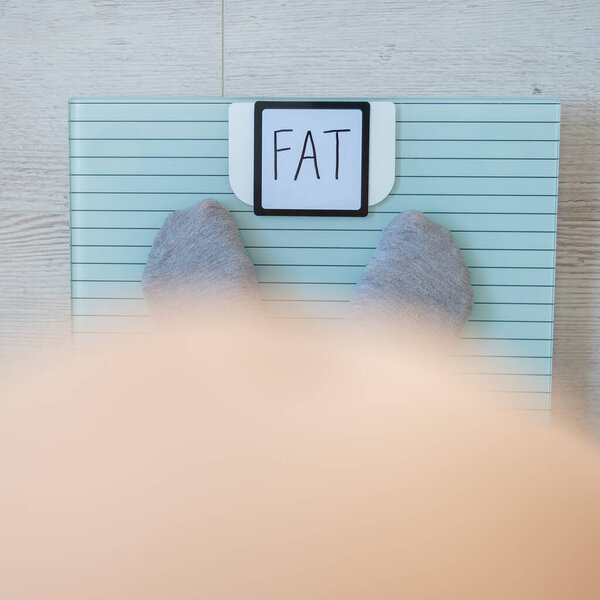 Top view of womens feet in gray socks on a floor scale. The inscription on the screen is fat. An obese man measures his weight. Naked big belly.