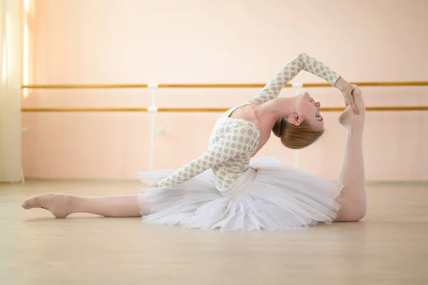 Prachtige ballerina in lichaam en witte tutu traint in een dansles. jonge flexibele danser poseren in pointe schoenen zitten op de vloer. — Stockfoto