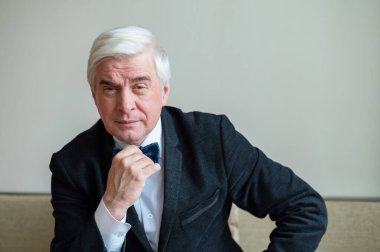 Takım elbiseli, papyonlu ve koltukta oturan kendine güvenen gri saçlı bir iş adamı. Üst düzey erkek patron ofiste..