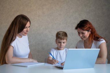 İki kadın çocuğa okul ödevinde yardım ediyor. Bayan öğretmen, evde bir çocuğa mutfakta ders veriyor. Öğretmen bireysel bir ders veriyor. Anne oğlunun çalışmasına yardım eder..