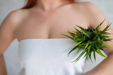 Yakın plan. Kırpılmış. Beyaz havluyla gezen bir kadın saksıda koltuk altı tutuyor ve vücudunda istenmeyen bitkiler var. Depilasyon. Koltuk altında kıllar alınıyor. Epilasyondan sonra pürüzsüz cilt.