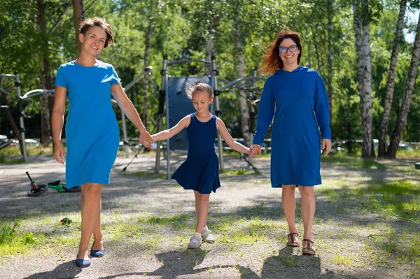 Гомосексуальная лесбийская пара держит дочерей за руки. Девушка гуляет с двумя матерями в парке. Две замужние женщины и ребенок на улице. — стоковое фото