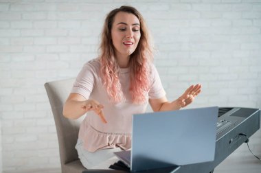 Dost canlısı bir kadın elektronik piyano çalıyor ve dizüstü bilgisayarında bir video blogu yönetiyor. Evde kal. Müzik enstrümanı öğretmeni. Uzaktan öğrenme müziği karantinaya alındı.