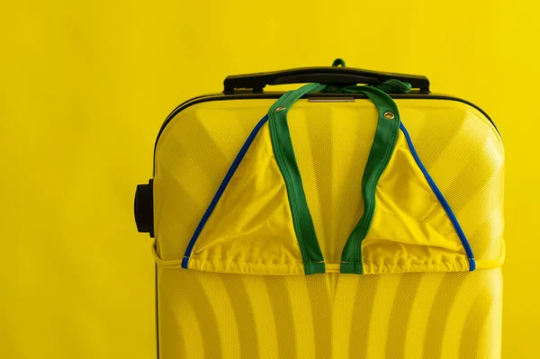 노란 배경 여행 가방에 여성 비키니. 여름 방학은 바다에서 보낸다. 스튜디오 안에 있는 수영복과 가방의 배합. — 스톡 사진