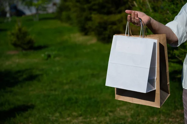 Close-up hands of an elderly woman with eco friendly paper bags in the park. Grandma holds paper bags outside. Cropped photo.