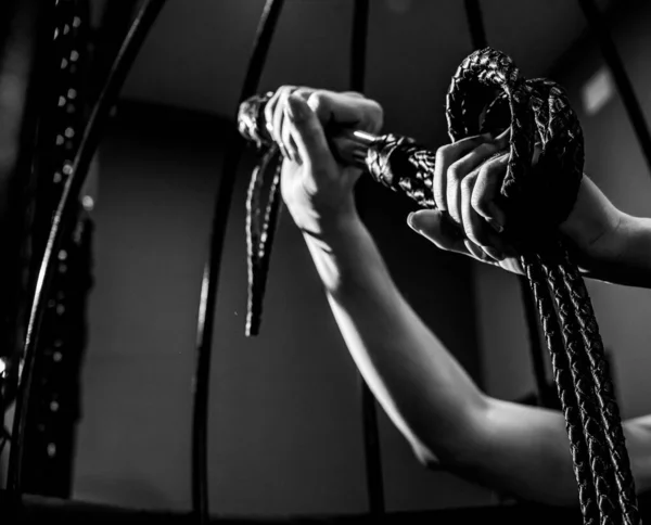 Mano femenina con una larga correa de cuero tejida en una jaula. BDSM Castigo y placer. Cultivado. — Foto de Stock