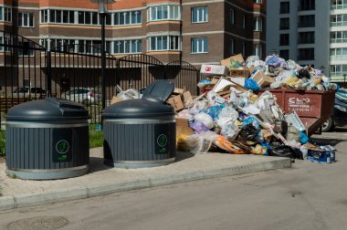 Bir apartmanın avlusunda kalabalık çöp tenekeleri vardı. Çöp konteynerleri. Çöpler kaldırıma saçılmış..