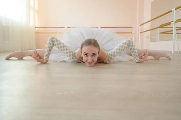 Hermosa bailarina en cuerpo y tutú blanco está entrenando en una clase de baile. Joven bailarina flexible posando en zapatos puntiagudos sentada en el suelo. —  Fotos de Stock