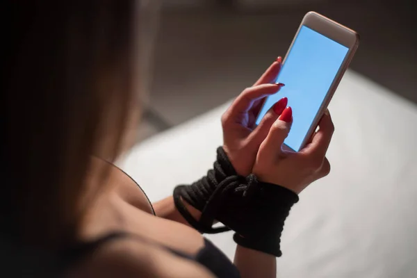 Una mujer en ropa interior de encaje está sentada en la cama con las manos atadas y sosteniendo un teléfono móvil. Chica sin rostro representa una adicción a los teléfonos inteligentes . —  Fotos de Stock