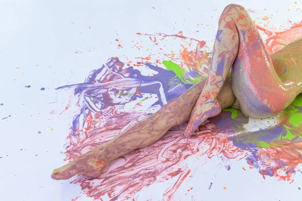 Γυμνή γυναίκα με λεκέδες από μπογιά σε λευκό πάτωμα. Θέα από ψηλά. Ψιλοκομμένο. Χρωματικές πιτσιλιές στο δέρμα. Ζωγραφική σώματος τέχνης. — Φωτογραφία Αρχείου