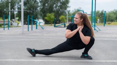 Obez genç beyaz kadın yan hamleler yapıyor. Siyah eşofmanlı şişman, güzel, gülümseyen kız dışarıda spor yapıyor. Eğitimden önce ısınıyorum..