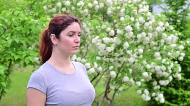 Güzel kızıl saçlı kadın hapşırır ve parkta çiçek açan bir elma ağacının yanında dururken burnunu ovuşturur. Mevsimsel alerjik rhinitis. Kızın polene alerjisi var..
