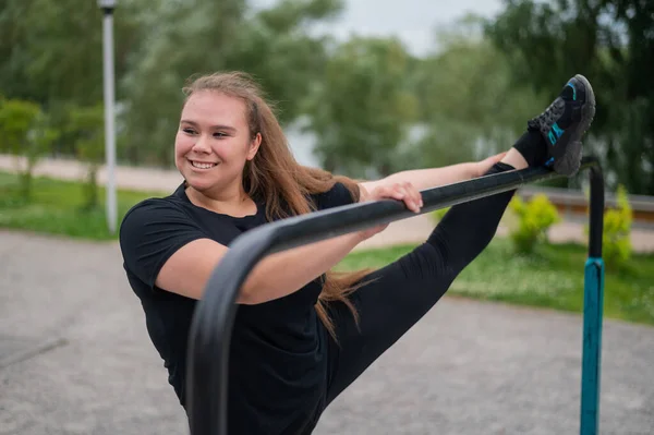 Dicke Mädchen dehnen sich auf den unebenen Stangen auf dem Spielplatz. Schöne junge lächelnde übergewichtige Frau beim Sport zur Gewichtsabnahme im Freien. — Stockfoto