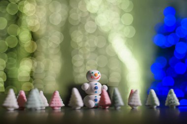 Tatlı kardan adam ve Noel ışıklarının arka planında marşmelovdan yapılmış küçük Noel ağaçları. Ağaçtaki ampullerden bir çelenk. Mutlu yıllar..