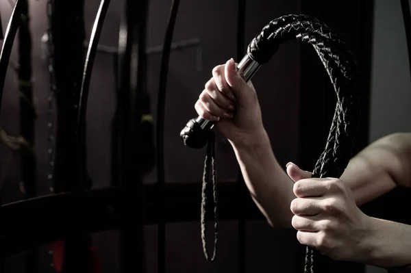 Female hand with a long woven leather lash in a cage. BDSM Punishment and pleasure. Cropped. — Stock Photo, Image