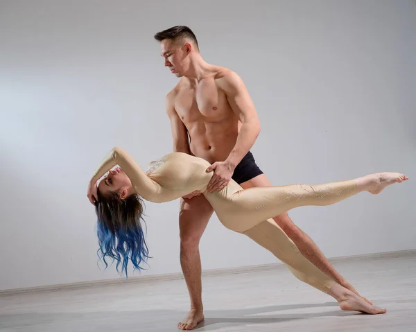 Casal acromático executar o número em um fundo branco. Um dueto de ginastas ensaiando uma performance com apoio. Um homem e uma mulher muito flexível estão dançando. — Fotografia de Stock