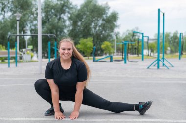 Obez genç beyaz kadın yan hamleler yapıyor. Siyah eşofmanlı şişman, güzel, gülümseyen kız dışarıda spor yapıyor. Eğitimden önce ısınıyorum..