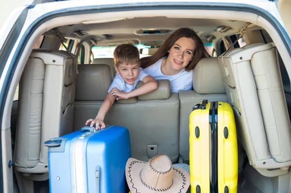 Glückliche Europäerin mit ihrem kleinen Sohn blickt auf den Kofferraum eines Autos mit Koffern. Sommerurlaub für die Familie. Mit einem Kind im Auto unterwegs. Ein Junge mit seiner Mutter auf dem Rücksitz eines Jeeps. — Stockfoto