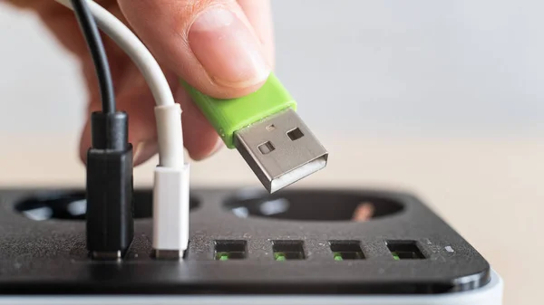 Modern bekväm multi-port usb laddare för enheter. Närbild av en kvinnlig hand pluggar flerfärgade kablar i ett eluttag. Makro. — Stockfoto