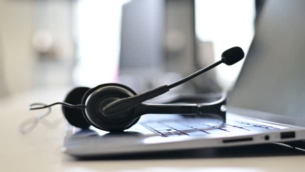 Close-up van een callcenter operators desktop. Zakelijke vrouw zonder gezicht die een headset van een laptop toetsenbord neemt. Het begin van de werkdag van een kantoormedewerker. — Stockvideo