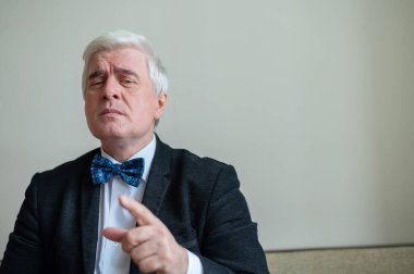 Takım elbiseli, papyonlu, beyaz saçlı, ciddi bir adamın portresi. Zarif giyimli, temiz tıraşlı bir son sınıf öğrencisi kameraya özgüvenle bakar ve parmağını gösterir. Hareketlendirme.