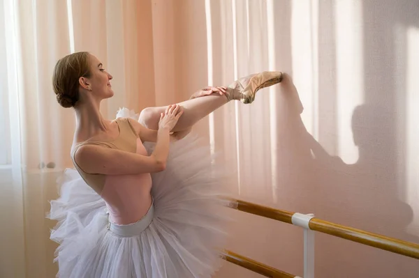 Die schöne anmutige Ballerina übt im Saal vor dem Hintergrund eines Fensters. Schlanke Frau in Tutu und Spitzenschuhen in einem Tanzkurs. — Stockfoto