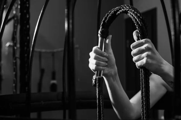 Vrouwelijke hand met een lange geweven leren zweep in een kooi. BDSM Straf en plezier. Gehakt. — Stockfoto
