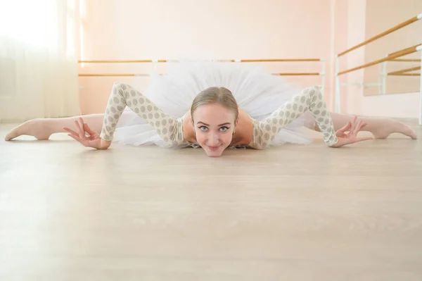 Beautiful ballerina in body and white tutu is training in a dance class. Young flexible dancer posing in pointe shoes sitting on the floor. — Stock Photo, Image