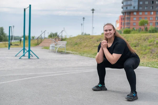 Dicke Mädchen betreiben Fitness auf dem Sportplatz. Schöne junge lächelnde übergewichtige Frau hockt draußen. Schlechte Essgewohnheiten. Übungen auf die Muskeln des Gesäßes. — Stockfoto