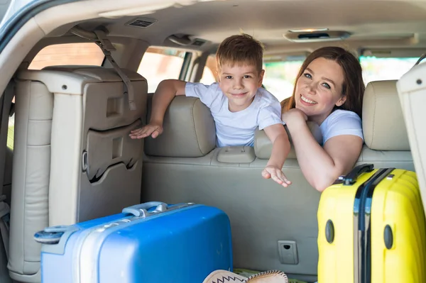 Glückliche Europäerin mit ihrem kleinen Sohn blickt auf den Kofferraum eines Autos mit Koffern. Sommerurlaub für die Familie. Mit einem Kind im Auto unterwegs. Ein Junge mit seiner Mutter auf dem Rücksitz eines Jeeps. — Stockfoto
