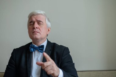 Takım elbiseli, papyonlu, beyaz saçlı, ciddi bir adamın portresi. Zarif giyimli, temiz tıraşlı bir son sınıf öğrencisi kameraya özgüvenle bakar ve parmağını gösterir. Hareketlendirme.