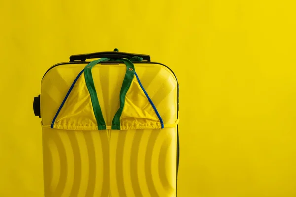 एक पीले पृष्ठभूमि पर एक सूटकेस पर महिला बिकनी। समुद्र में गर्मियों की छुट्टियों के लिए सेट करें। स्टूडियो में एक तैराकी सूट और बैग की संरचना . — स्टॉक फ़ोटो, इमेज