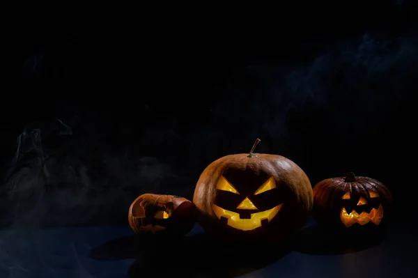 Trzy przerażające halloween parujące dynie z wyrzeźbionym świecącym uśmiechem na czarnym tle. Ręcznie robiona głowa Jacka-o-latarni ze świecą wewnątrz w ciemności pośród mgły. Cukierek albo psikus. Pocztówka. — Zdjęcie stockowe