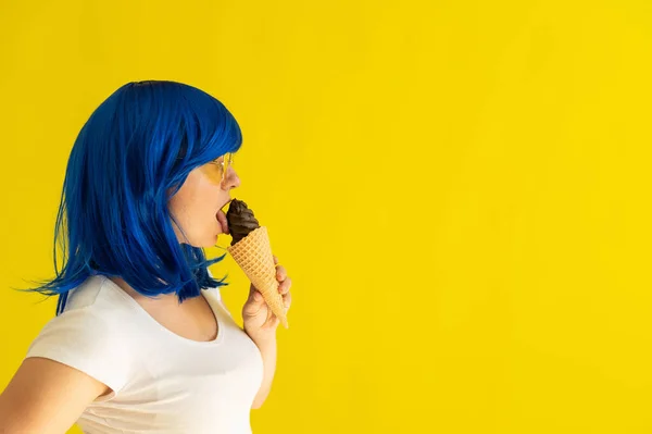 파란색 머리카락을 가진 여자가 노란 배경에 있는 와플 콘에서 아이스크림을 성적으로 핥는다. 가발 과 선글라스를 낀 소녀는 스튜디오에서 초콜릿 젤라토를 즐겨 먹는다. — 스톡 사진
