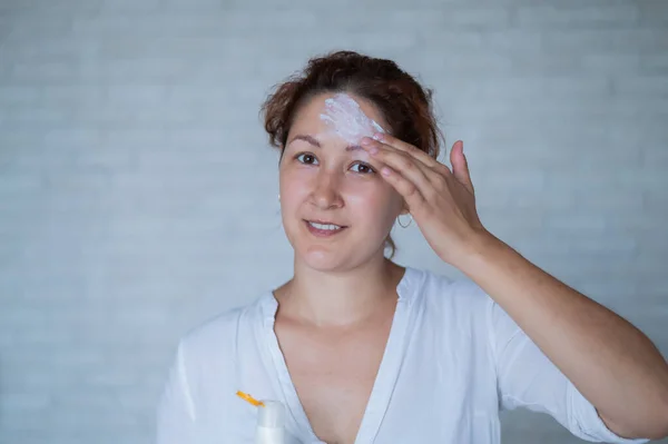 Vitiligo. Retrato de una mujer sin pigmentación de la piel en la frente. La chica mancha protector solar en una mancha blanca en la piel de la cara. Enfermedad autoinmune . — Foto de Stock