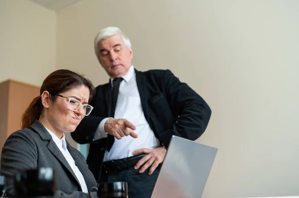 The male boss indicates the female subordinate a mistake. A gray-haired mature business man scolds an employee for unfulfilled work. An upset Caucasian woman failed.