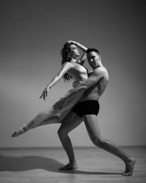 Un uomo e una donna stanno ballando balletto moderno. Coppia acrobatica eseguire il numero su uno sfondo bianco. Un duetto di ginnaste che provano una performance con supporto. Monocromatico foto. — Foto Stock