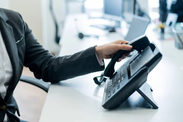 Primer plano mano femenina en el teléfono fijo en la oficina. Mujer sin rostro en un traje trabaja como recepcionista contestando el teléfono a las llamadas de los clientes. — Foto de Stock