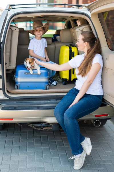 Europeisk kvinna med son och valp Jack Russell reser med bil. Grabben och hans mamma och en liten hund sitter i bagageluckan och åker ut på sommarsemester. Oberoende familjeresa med barn. — Stockfoto