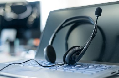 Çağrı merkezi operatörü masaüstü. Bir dizüstü bilgisayardaki kulaklığın yakın çekimi. Yardım masası. Destek servisi çalışanının işyeri. Bilgisayar klavyesindeki ses için mikrofonlu kulaklıklar..