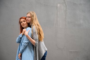 İki mutlu kız arkadaş gri bir duvarın arkasında sarılıyorlar. Lezbiyen bir bayana nazikçe sarılmak. LGBT Eşcinsel Evliliği.