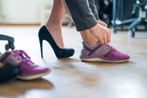 Close-up of legs of an office female employee with foot pain. A woman changes high black suede heels to more comfortable shoes. The girl takes off her shoes and puts on purple running shoes.