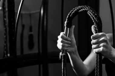 Kafeste uzun, dokunmuş deri kamçılı bir kadın eli. BDSM Ceza ve Zevk. Kırpılmış.